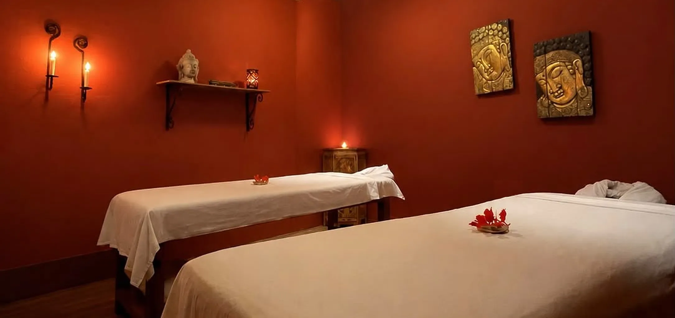 Two massage beds in a terracotta treatment room with candles and carved Buddha art
