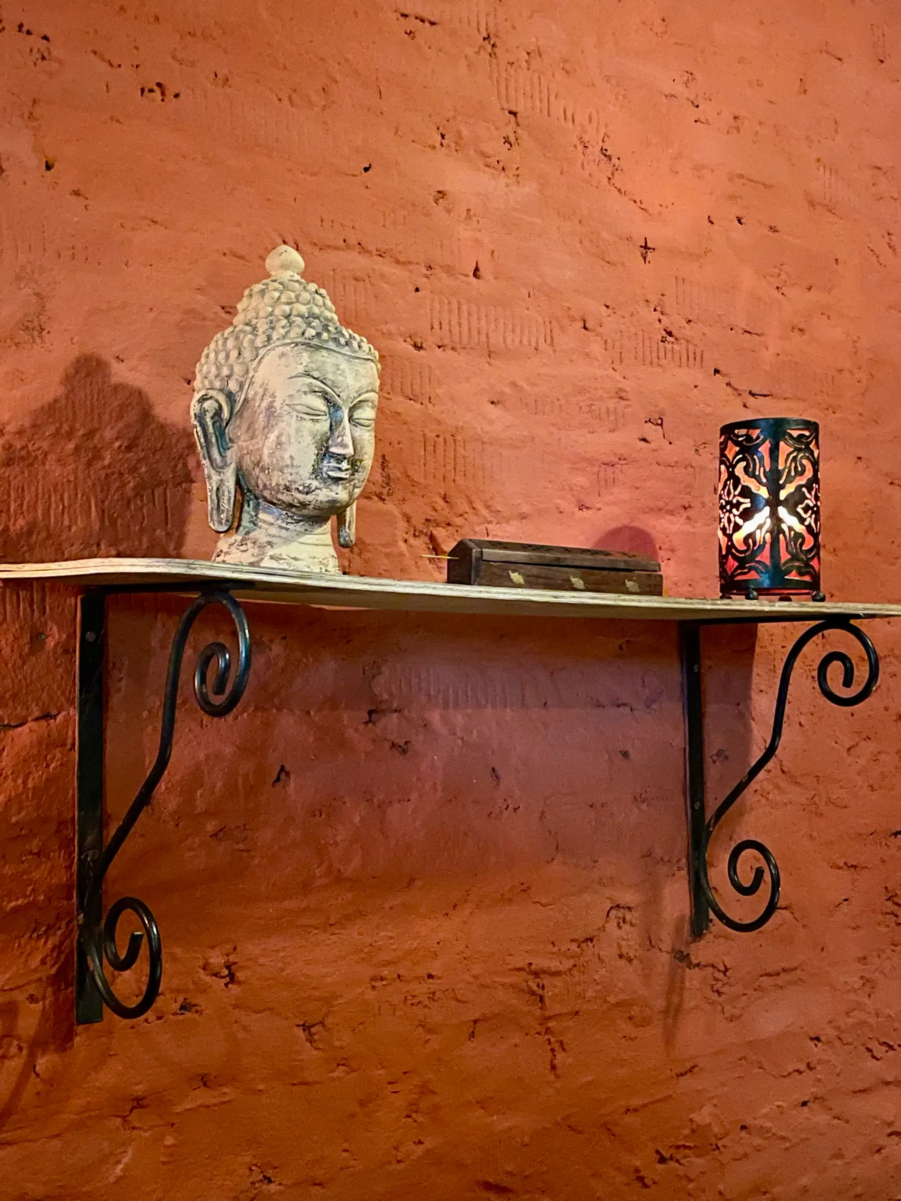 Stone Buddha head and lantern on a wrought-iron shelf